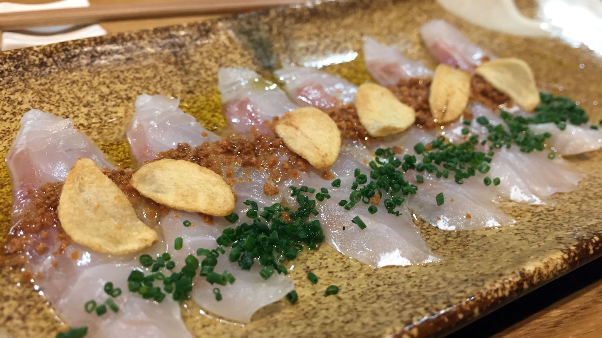 Wolfsbarsch-Sashimi mit geröstetem Knoblauch und Schnittlauch. Foto WR